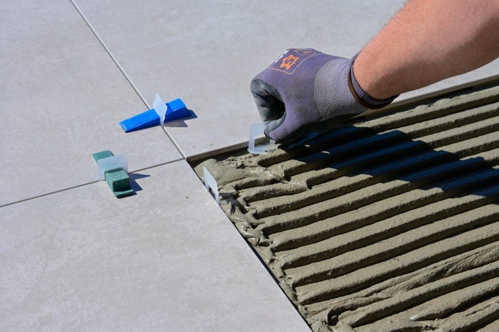 a-close-up-shot-of-a-person-putting-tile-levelers-11806490 Detailed view of gloved hand aligning tiles with levelers and spacers during construction.