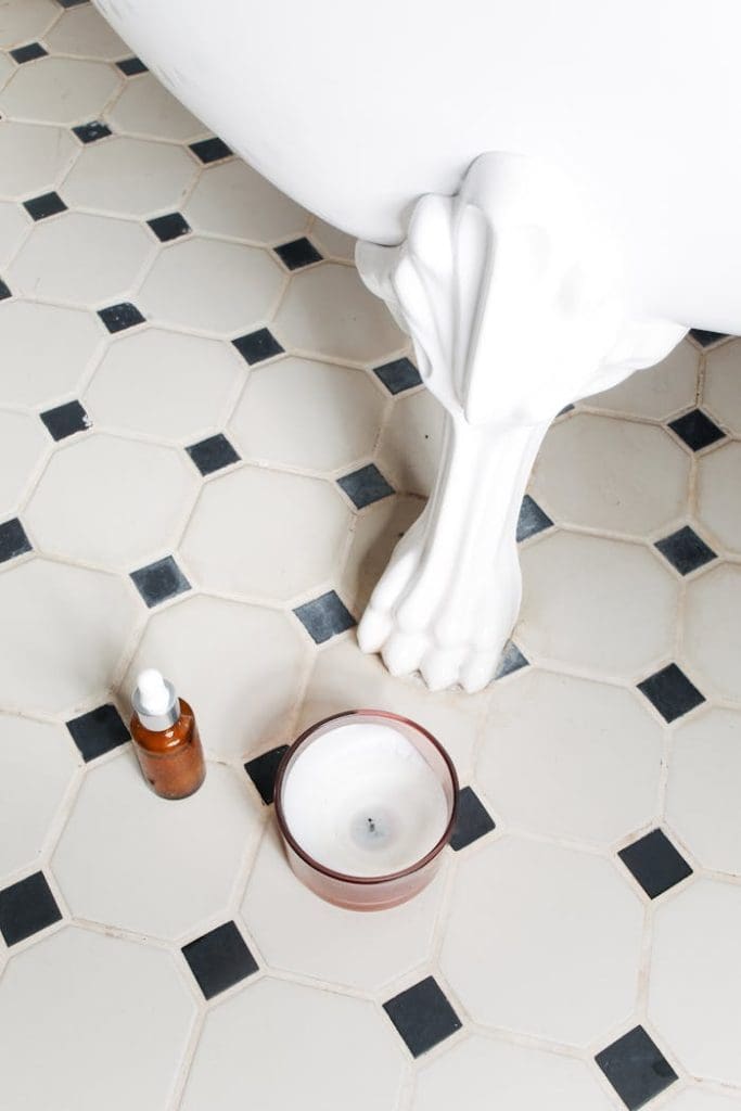bottle-of-beauty-product-and-a-candle-jar-on-the-floor-5849423 Decorative bathroom scene with classic bathtub and ceramic tile floor.