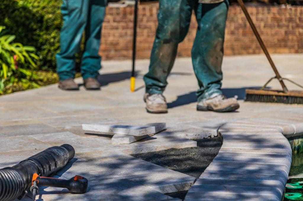 close-up-shot-of-tiled-ground-9690090 Workers laying tiles on an outdoor patio under sunlight.