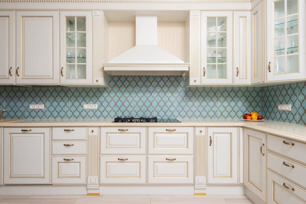 white-wooden-cabinets-of-expensive-kitchen-7045826 Interior of light modern kitchen with wooden white cabinets and blue tile backsplash with classic hood